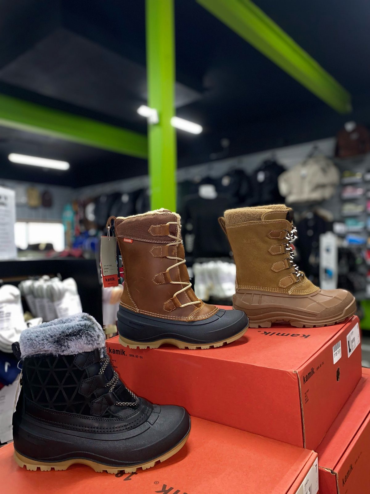 Three pairs of winter boots displayed on red boxes inside a retail store.