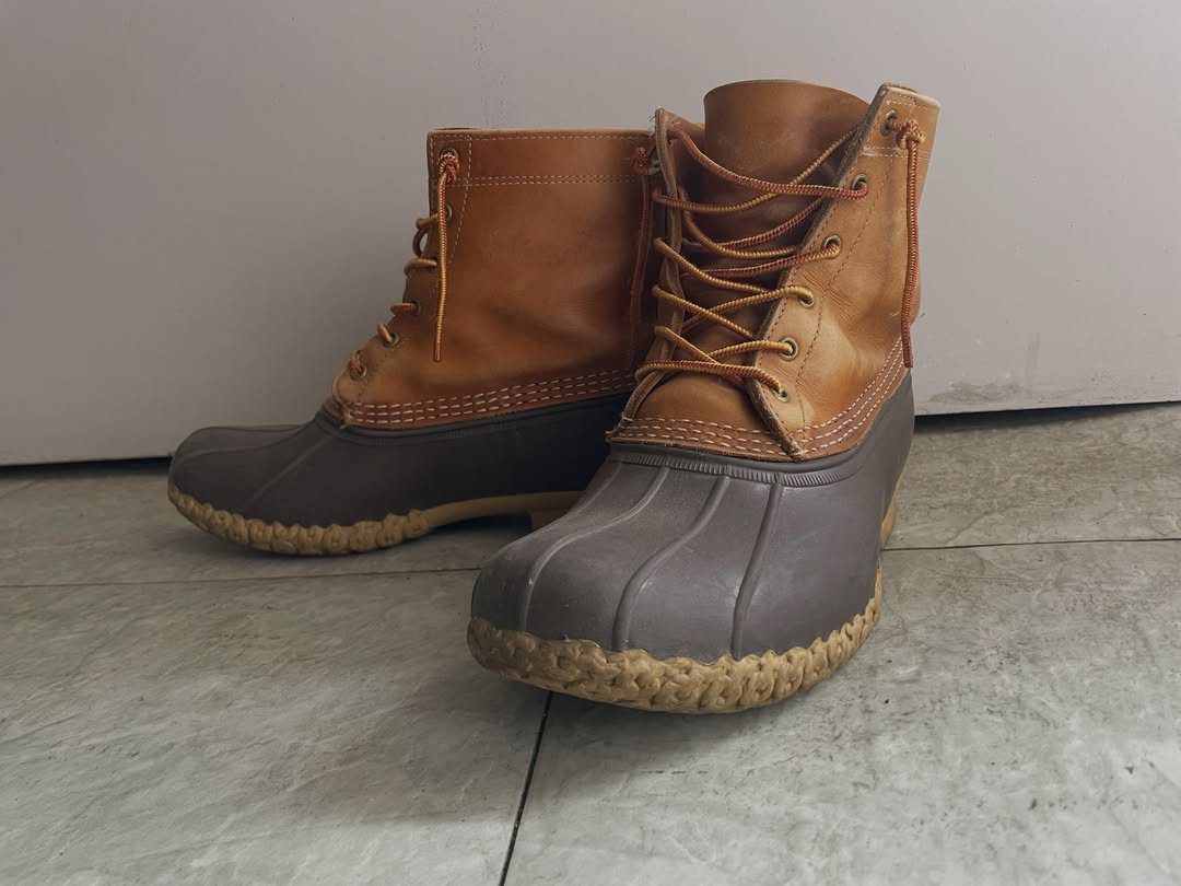 Tan leather and grey rubber duck boots resting on a grey tiled floor.