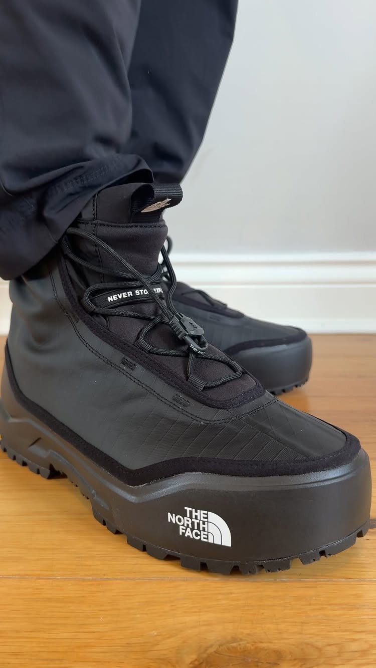 Black The North Face winter boots worn by a person on a wooden floor.