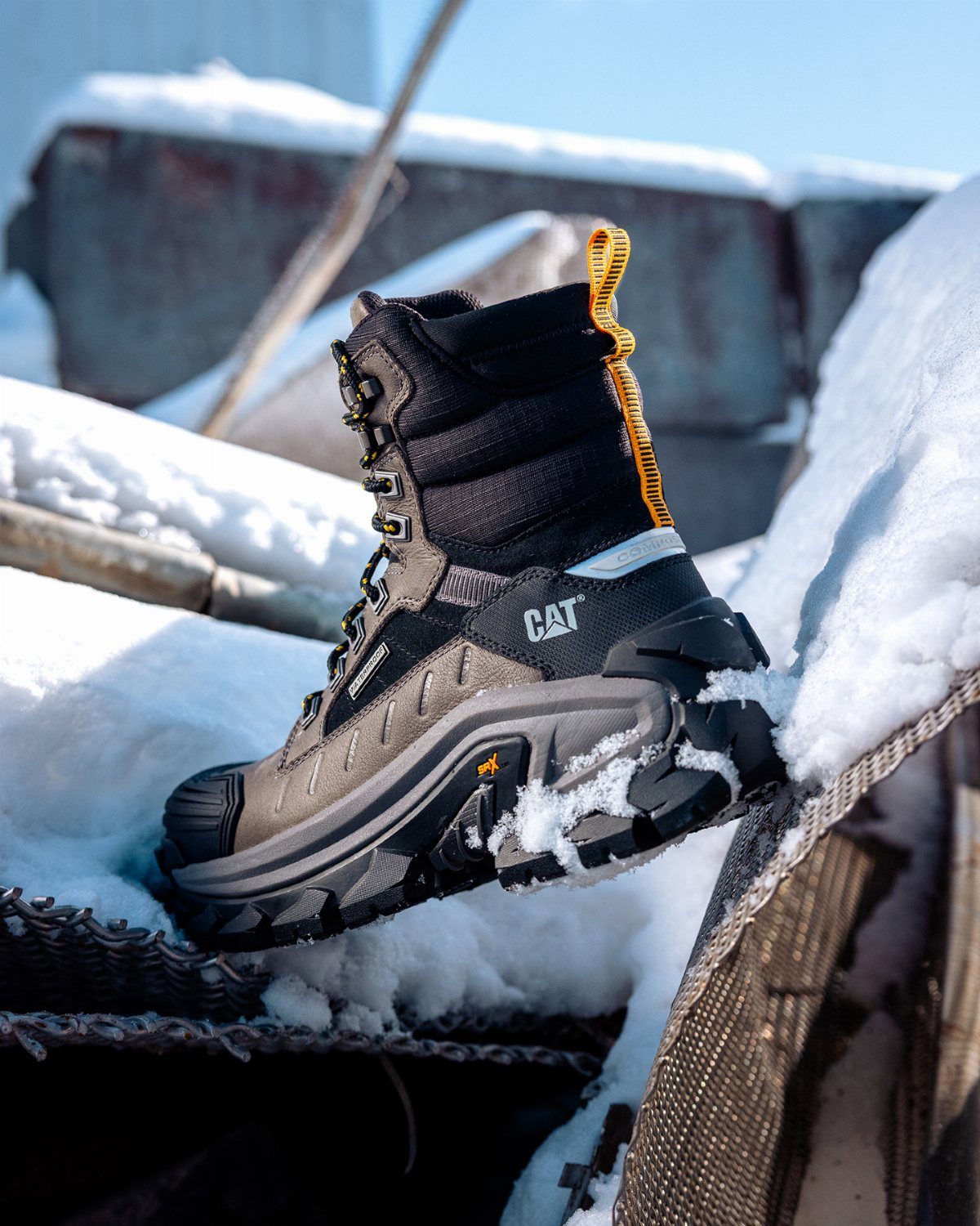 A black Caterpillar hiking boot resting in white snow on a metal structure.