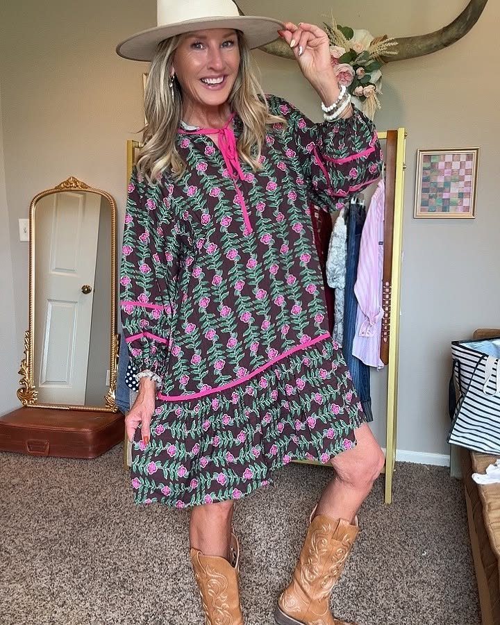 A woman posing in a floral patterned dress and tan cowboy boots wearing a hat.