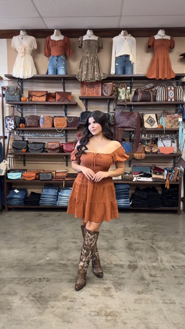 A woman posing in a rust-colored dress and patterned country boots inside a boutique.