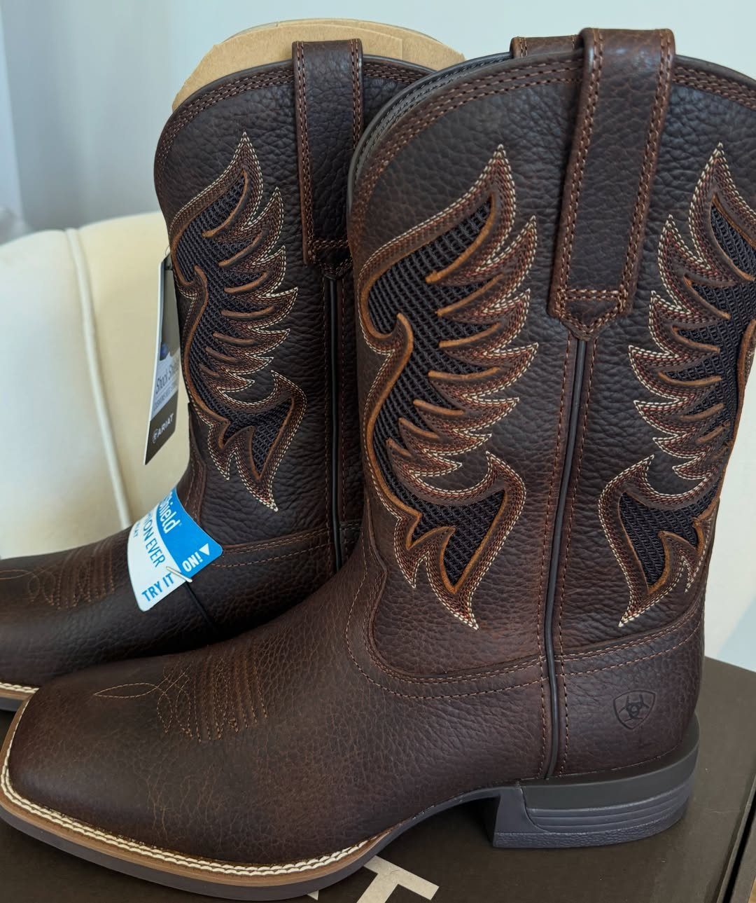 Two dark brown leather cowboy boots with intricate stitching and mesh side panels sitting on a surface.