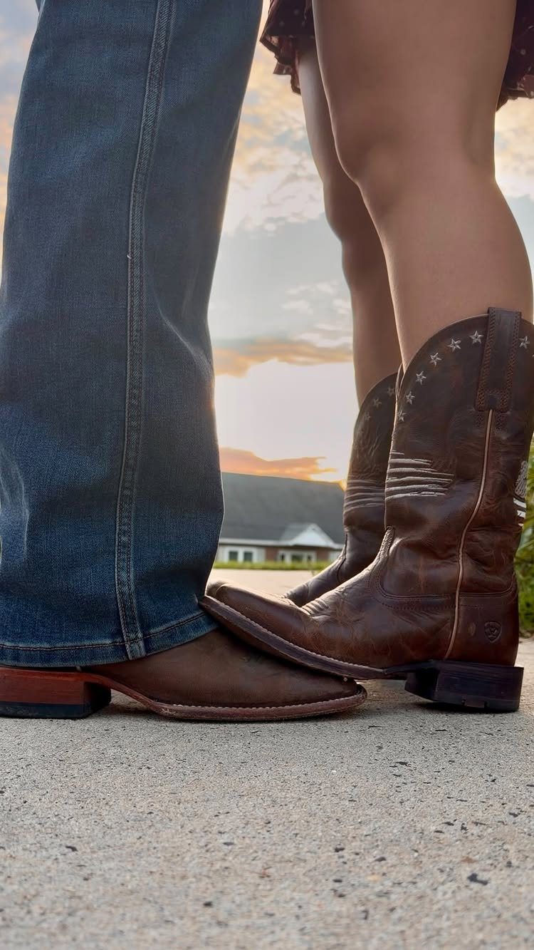 Brown leather cowboy and cowgirl boots standing on concrete against a sunset sky.