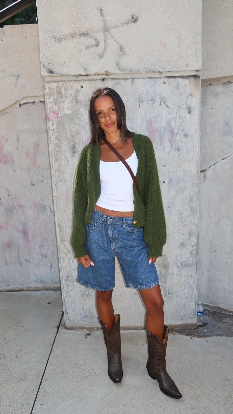 Woman wearing a white tank top, green cardigan, denim shorts, and brown cowboy boots.