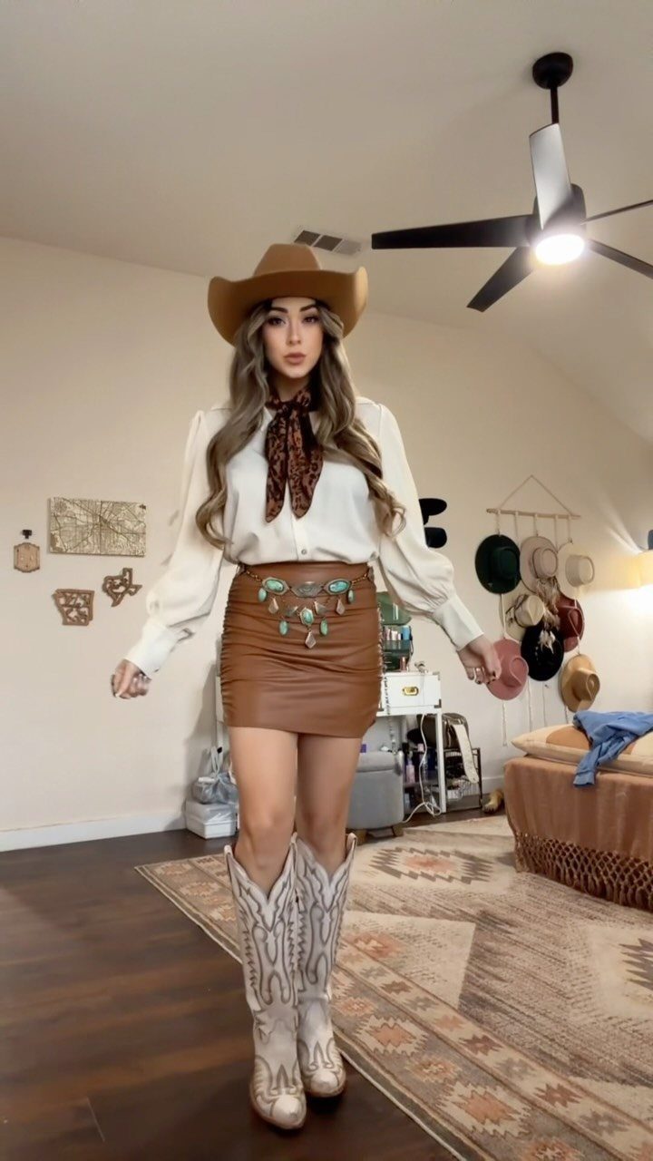 Woman in a cowboy hat, white blouse, leather mini skirt, and white cowboy boots.