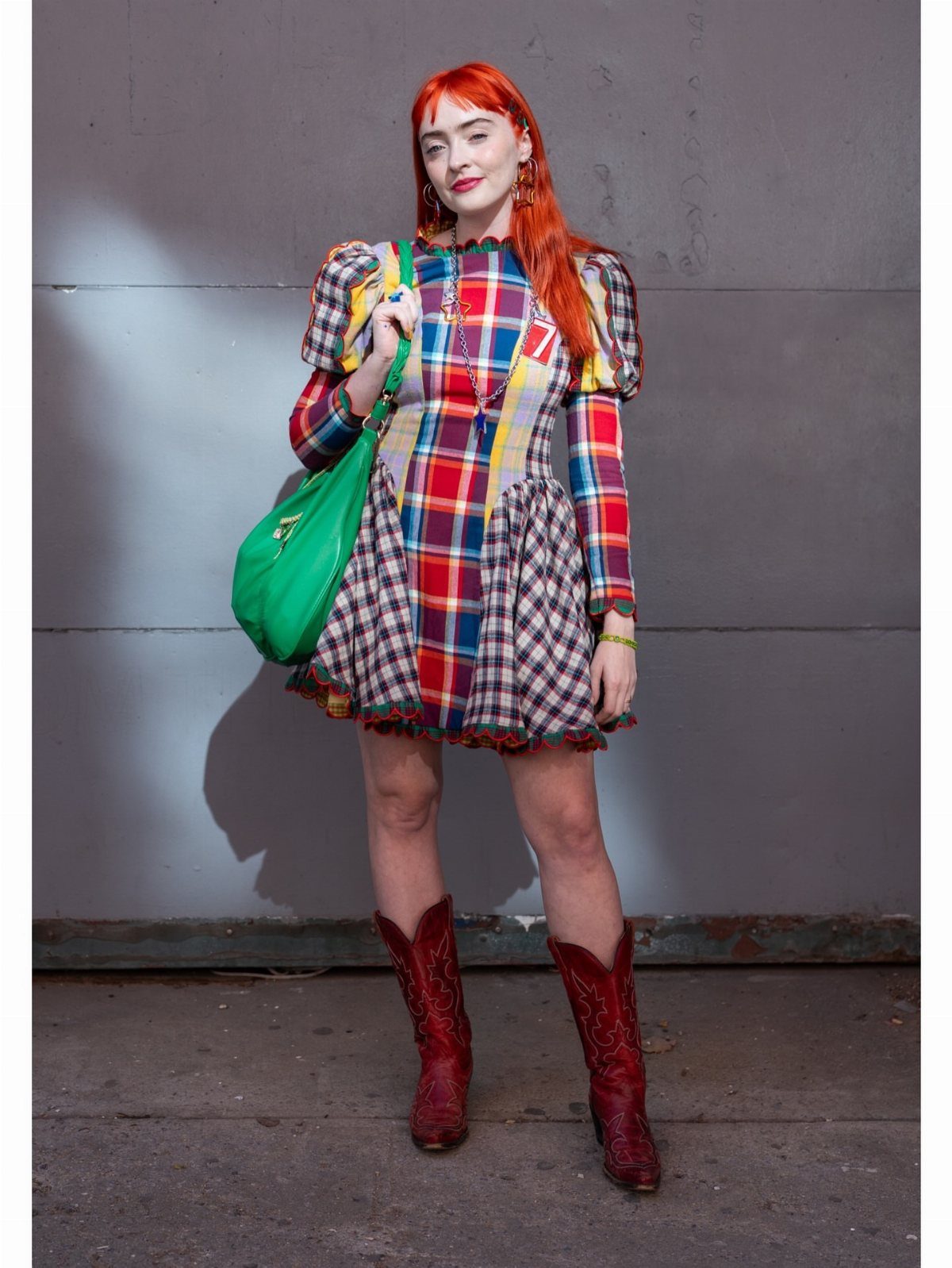 A woman with red hair wearing a colorful plaid dress and red cowboy boots.