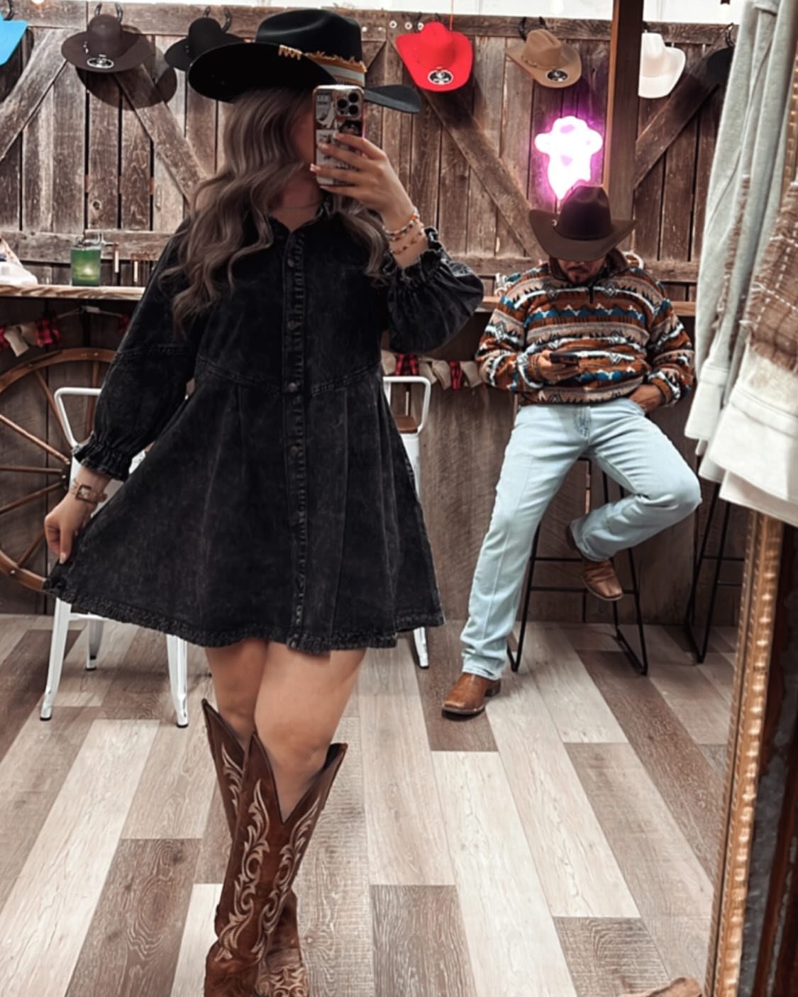 Woman in a black long-sleeved dress and brown cowboy boots taking a mirror selfie.