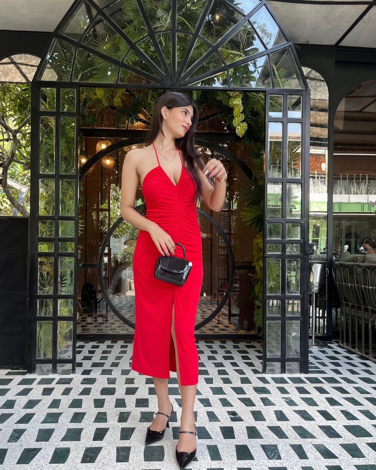 Woman in a red dress wearing black pointed-toe pumps standing in front of a glass building.