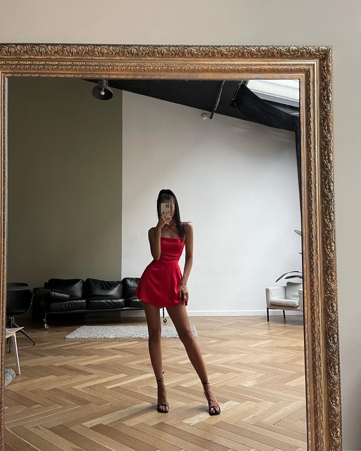 Woman in a red dress posing in a mirror wearing black strappy high heels.