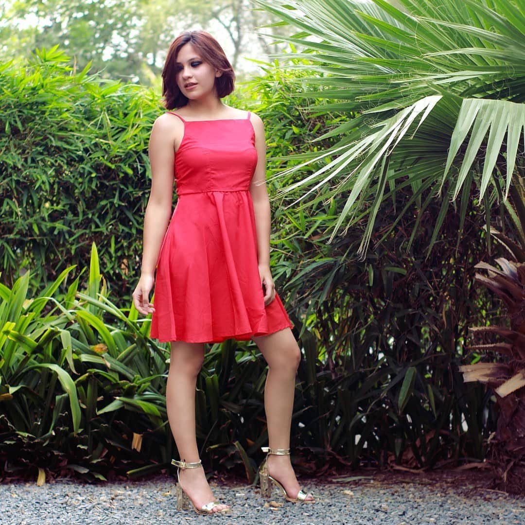 A woman in a red dress wearing gold metallic block heel sandals amidst green tropical plants.