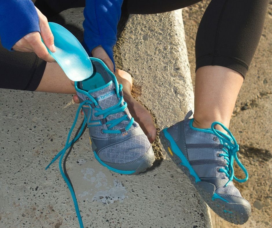 A person inserting a blue silicone heel cup into a grey athletic sneaker.