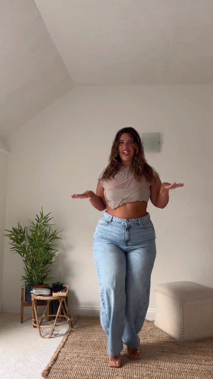 Woman posing in light blue high-waisted jeans, a beige crop top, and tan high heels.