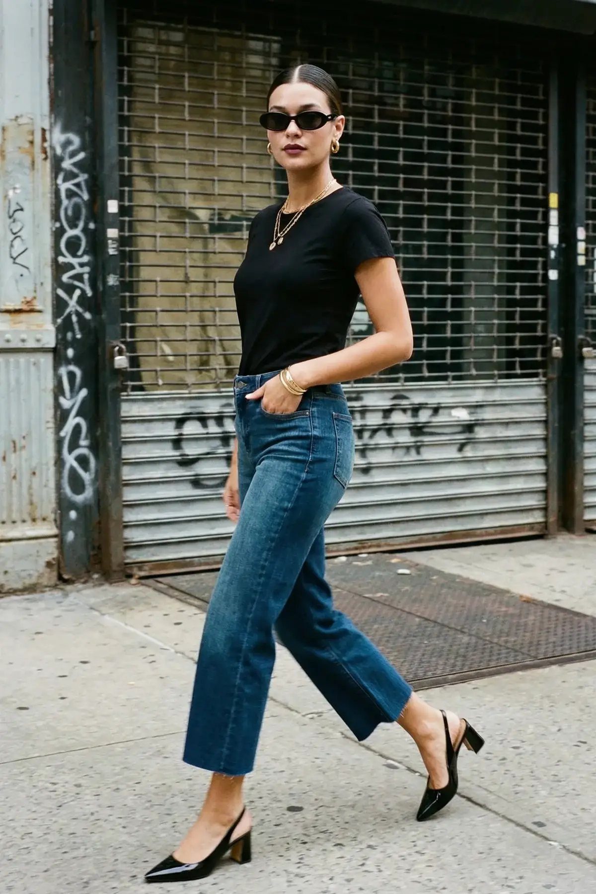 Woman walking in blue cropped jeans and black pointed-toe heels on a city street.