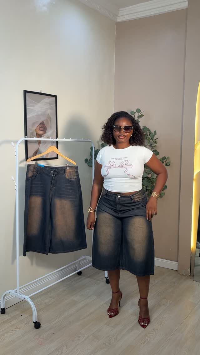 A woman posing in a white t-shirt, denim culottes, and red high heels.