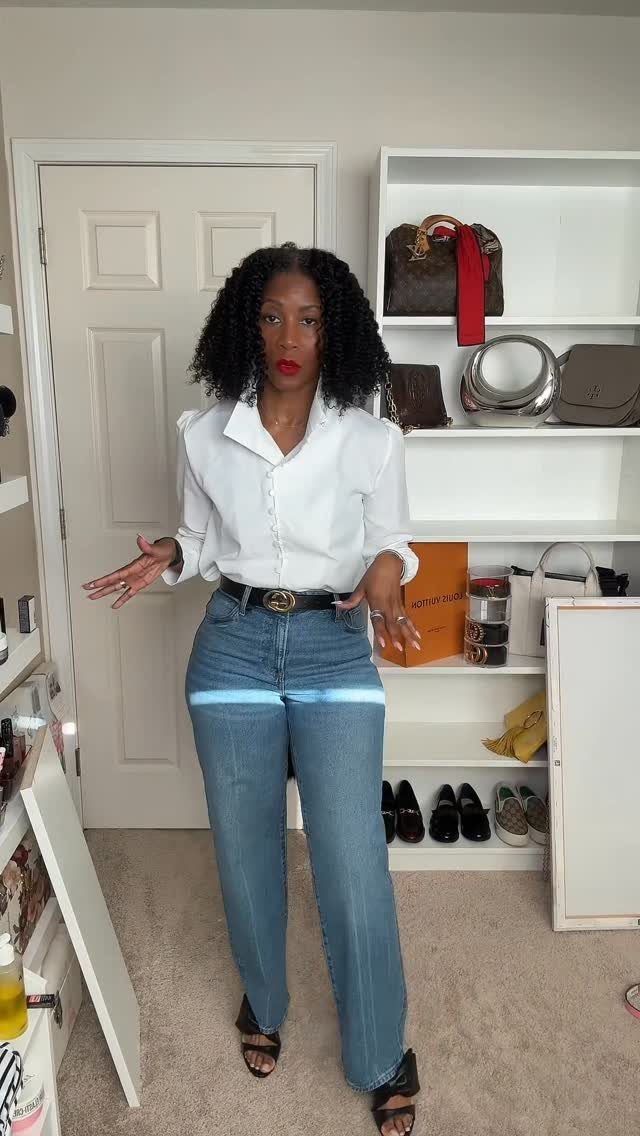 A woman wearing a white shirt, blue jeans, and black high heels standing in a room.