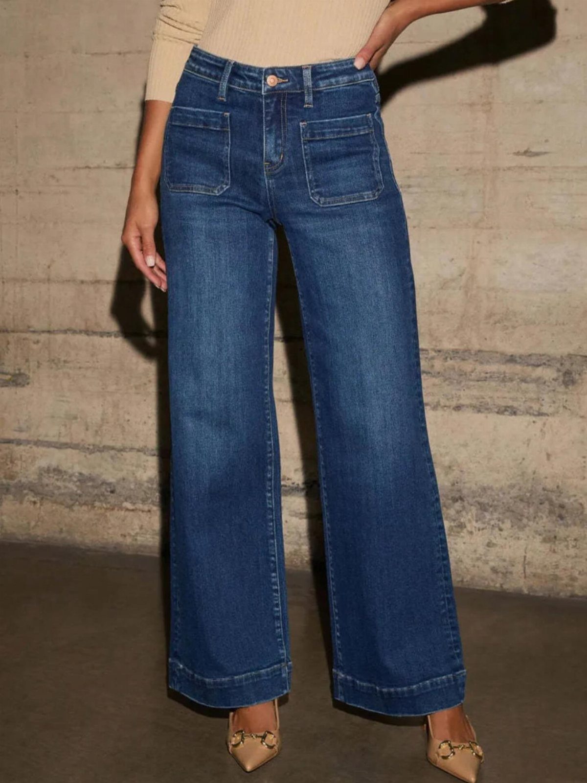Person wearing high-waisted wide-leg blue jeans, a beige tucked-in top, and tan heels.