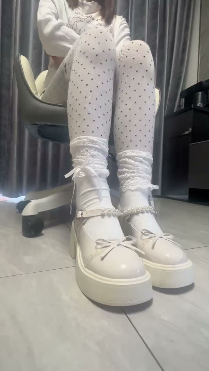 Person wearing white polka dot tights, lace ankle socks, and white platform Mary Jane heels.