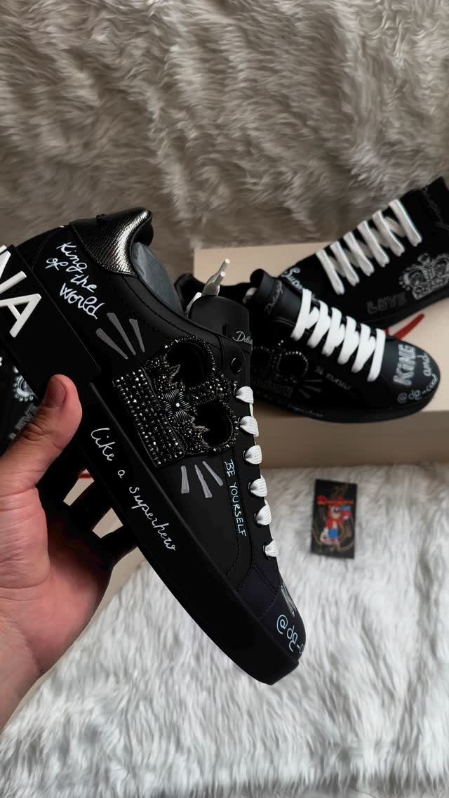 Black designer sneakers with skull details and white text held by a hand.