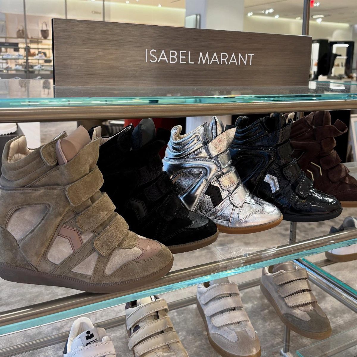 High-top wedge sneakers in beige, black, silver, and brown displayed on glass retail shelves.