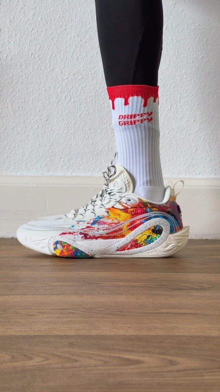 Colorful Li-Ning Mix Ace sneakers with paint splatter patterns worn with white socks on a wooden floor.