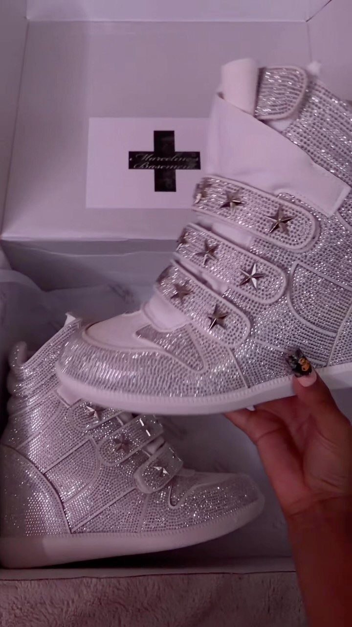 Silver glittery high-top sneakers with star embellishments being held over a white shoebox.
