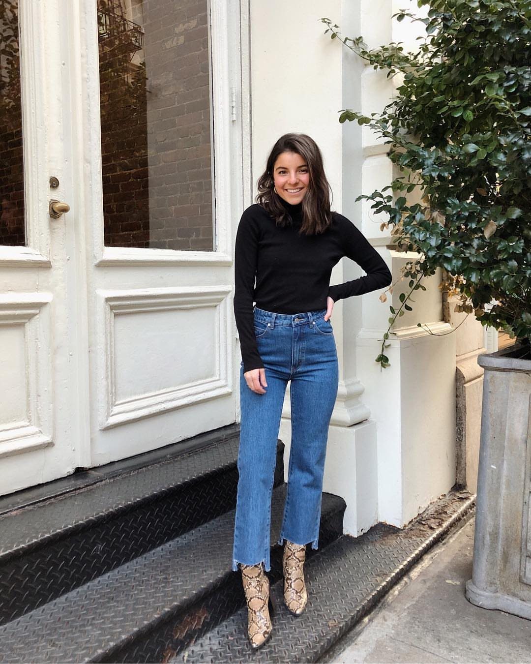 A woman wearing blue cropped jeans and snakeskin ankle boots standing on steps.