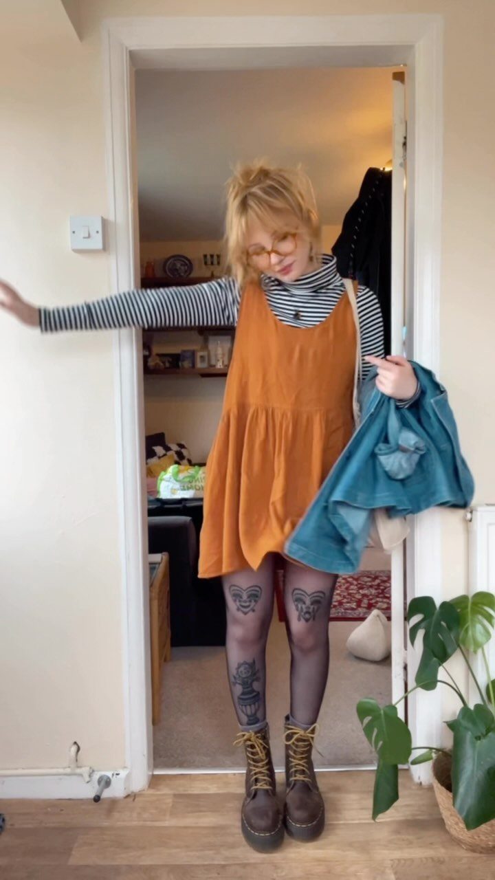 A person wearing an orange slipdress, striped top, patterned tights, and chunky platform boots.