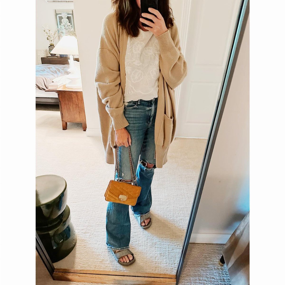 Person wearing blue jeans, white top, tan cardigan, and Birkenstock sandals standing before a mirror.