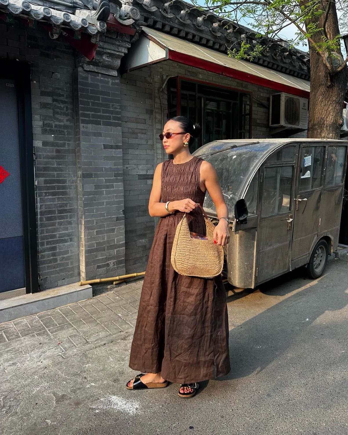 Woman in a brown maxi dress and black sandals standing on a city street.