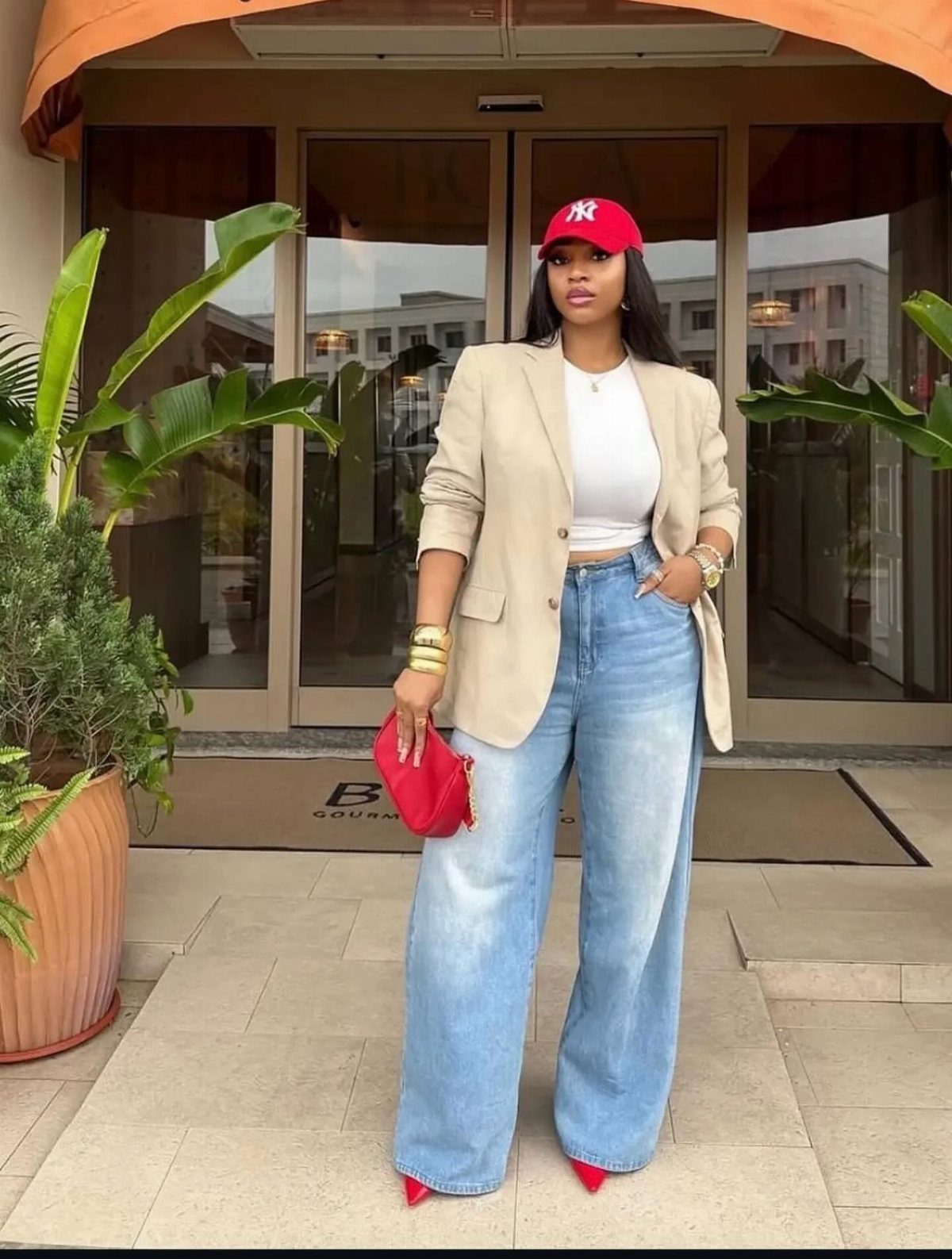 Woman wearing a beige blazer, white top, wide-leg jeans, and red accessories standing outdoors.