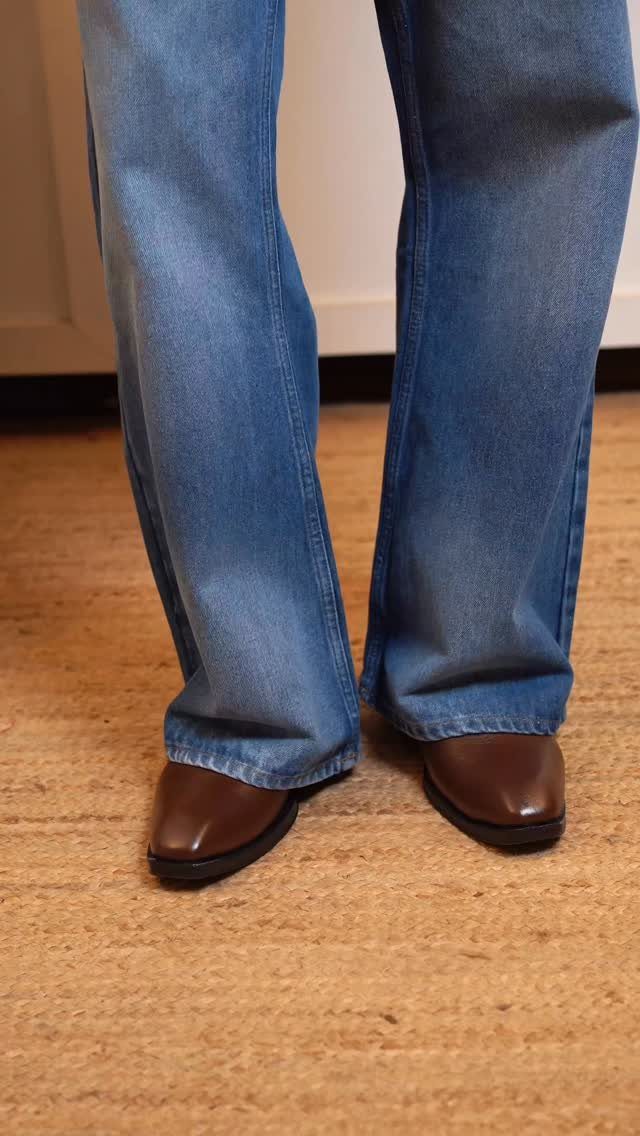 Blue flared jeans paired with brown leather Chelsea boots on a tan rug.