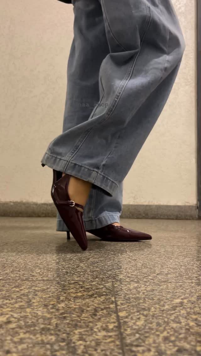 Person wearing baggy blue jeans and burgundy kitten heel pumps on a speckled floor.