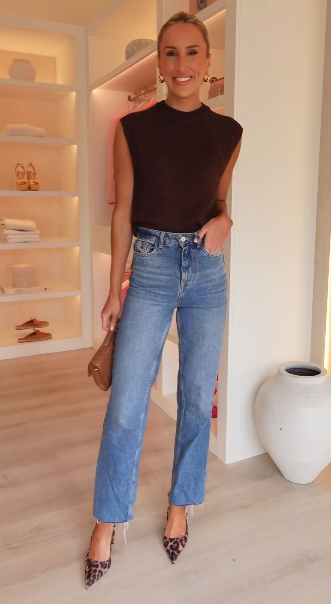 A woman wearing blue jeans and leopard print kitten heels standing in a closet.