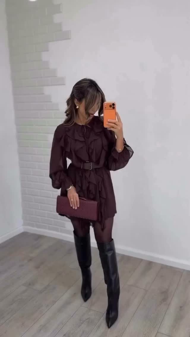 Woman in a burgundy ruffled mini dress and black knee-high boots taking a selfie.
