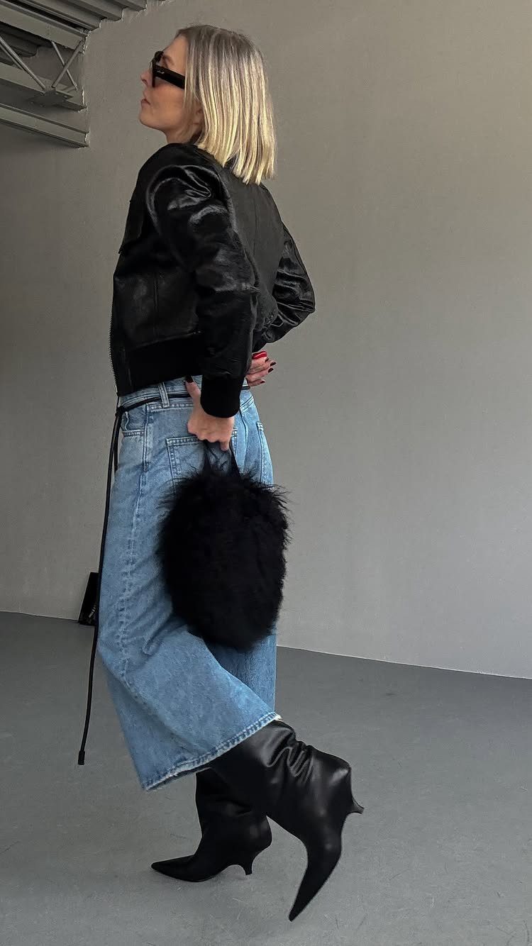 Blonde woman wearing a black leather jacket, denim culottes, and black knee-high boots.