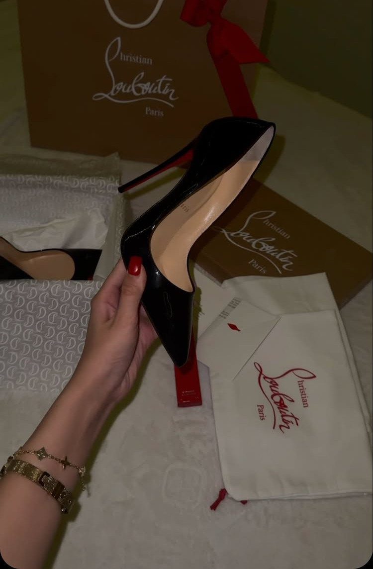 A hand holding a black patent leather high heel with a distinctive red sole.