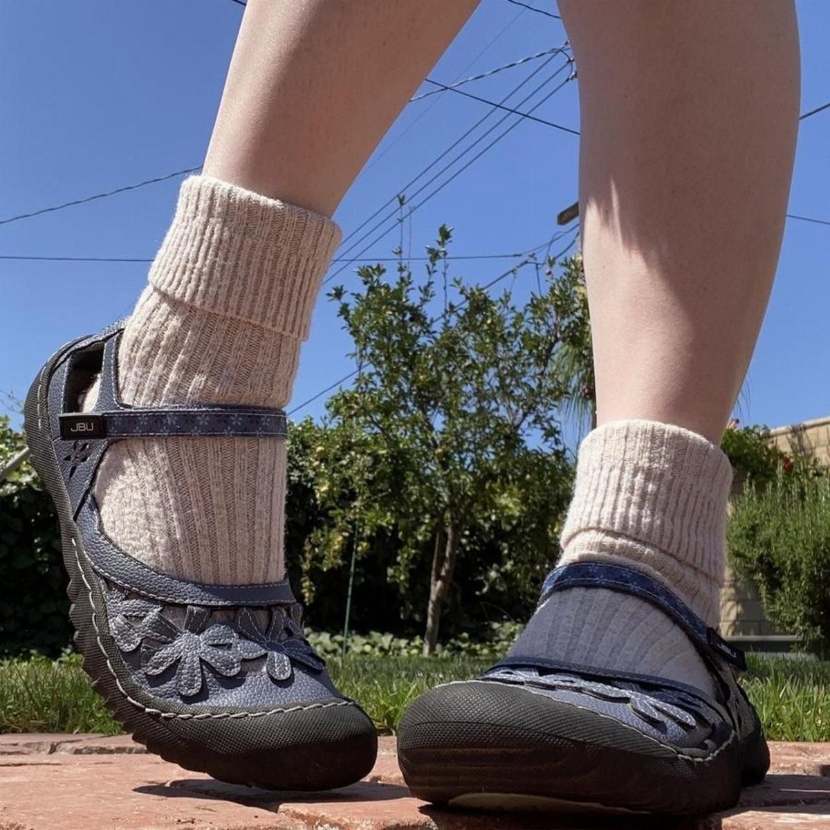 Person wearing dark blue floral Mary Jane shoes with thick beige ribbed crew socks outdoors.