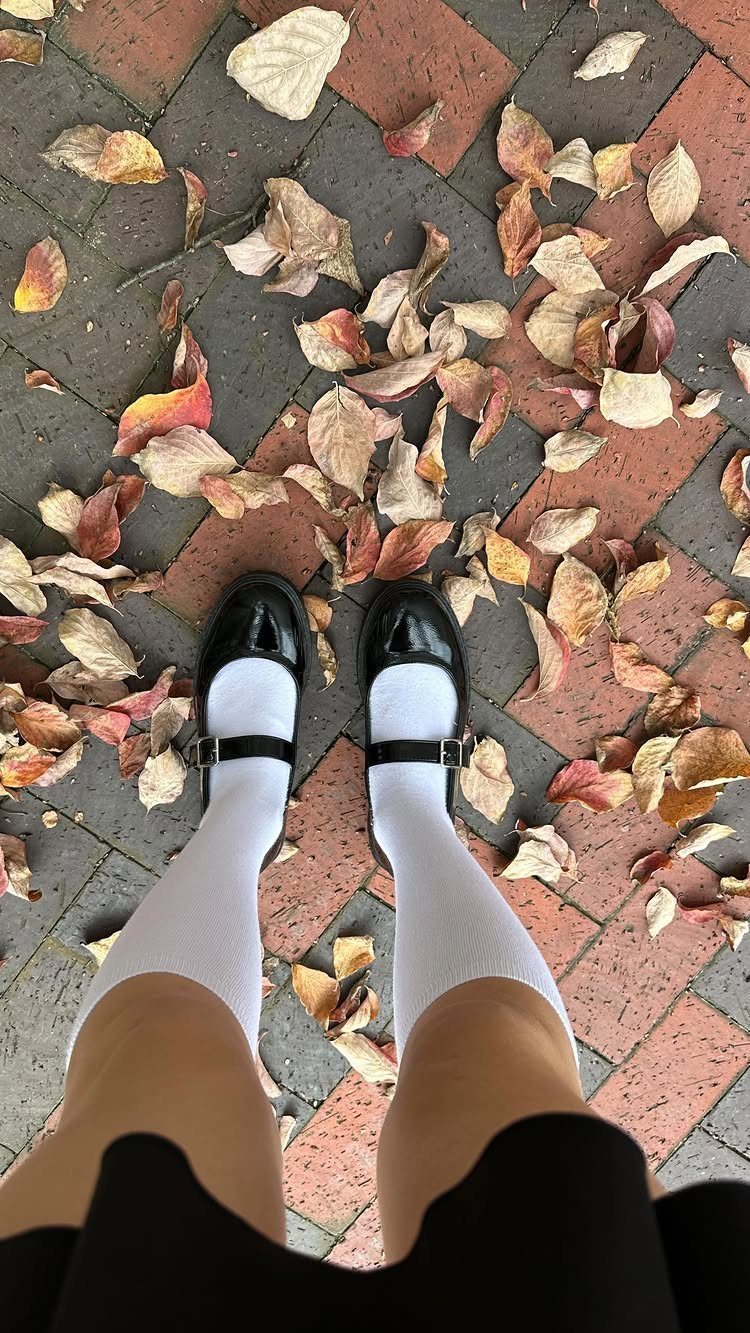 Person wearing black Mary Jane shoes and white knee-high socks standing on autumn leaves.