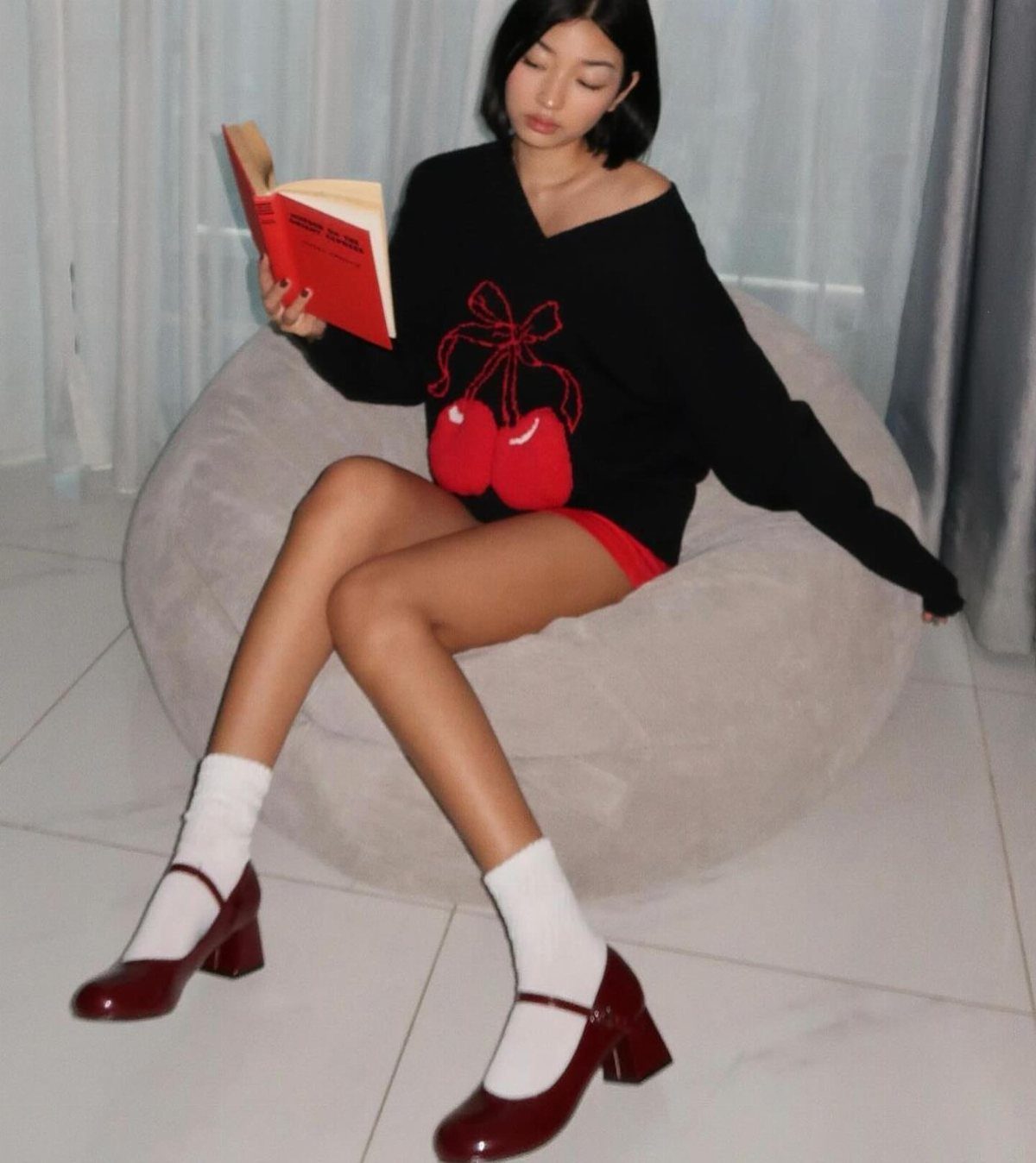 Woman in black cherry sweater sitting in a beanbag chair wearing white socks and red Mary Jane shoes.