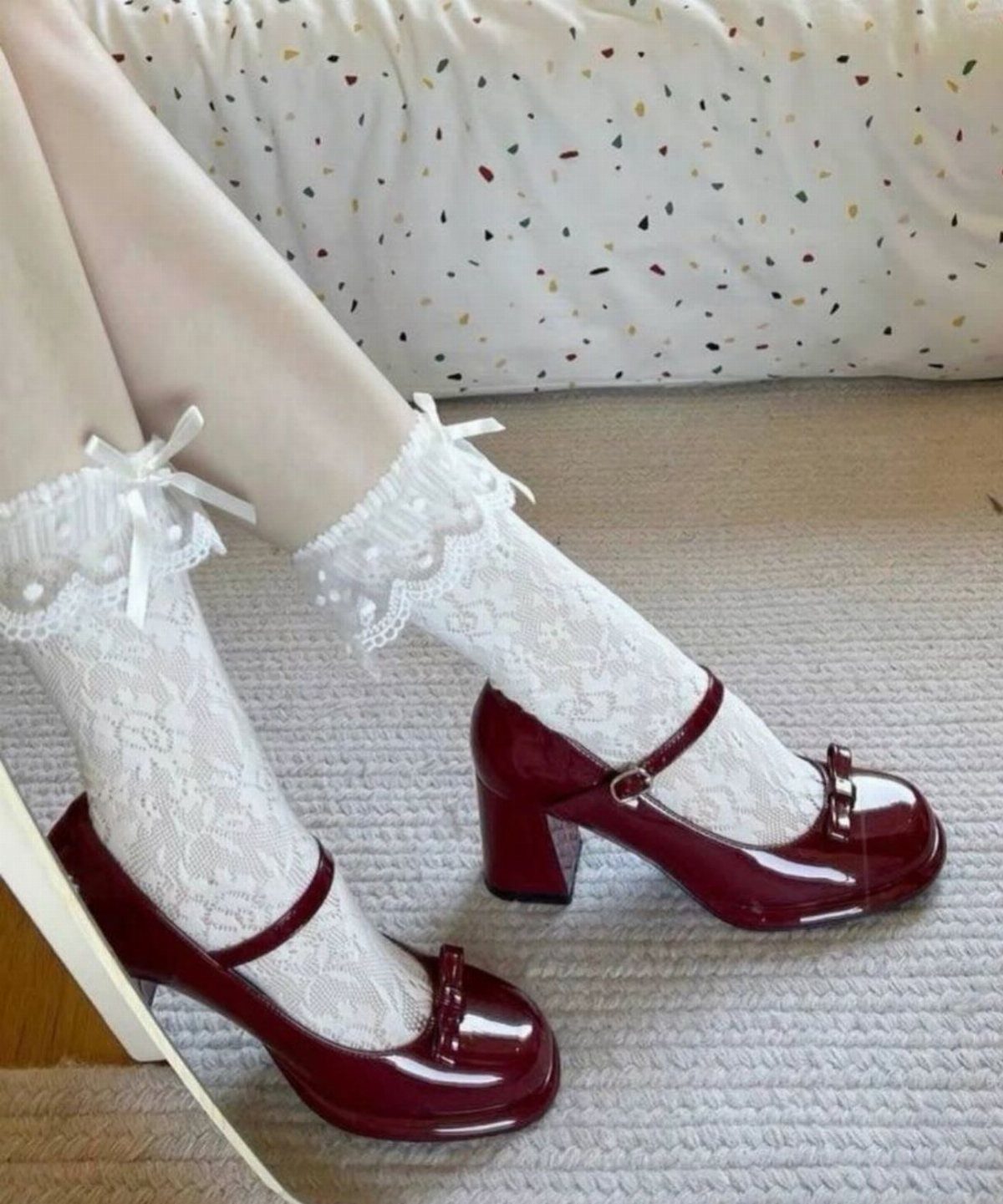 Legs wearing white lace ruffle socks and dark red patent leather Mary Jane shoes.