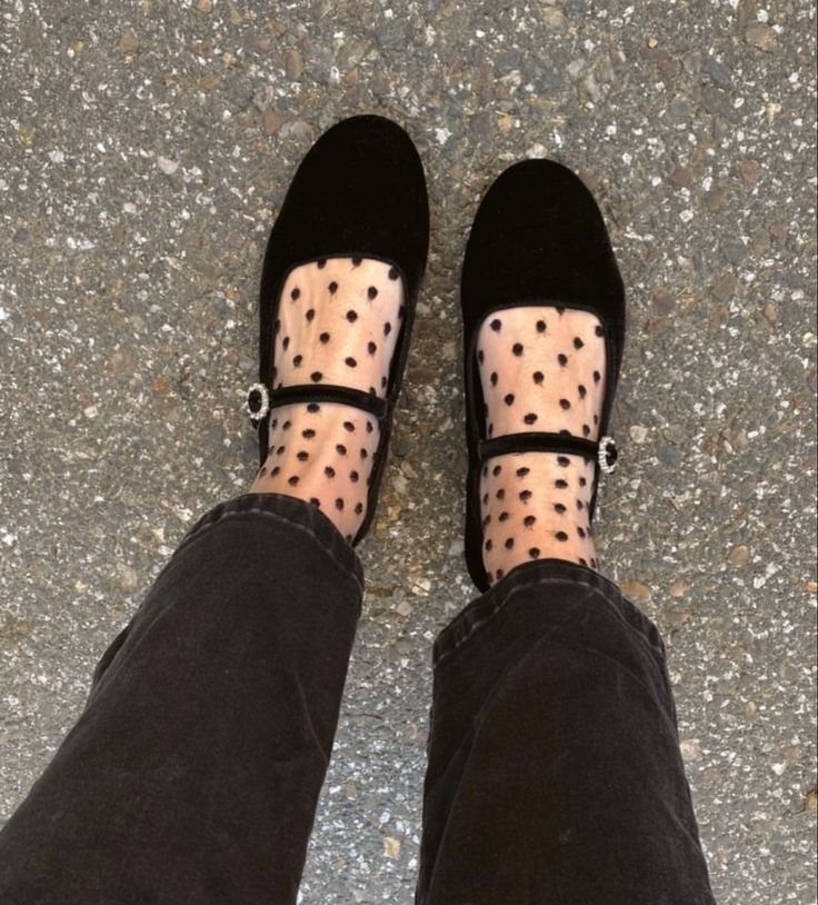 Black velvet Mary Jane shoes with polka dot sheer socks worn by a person standing on pavement.