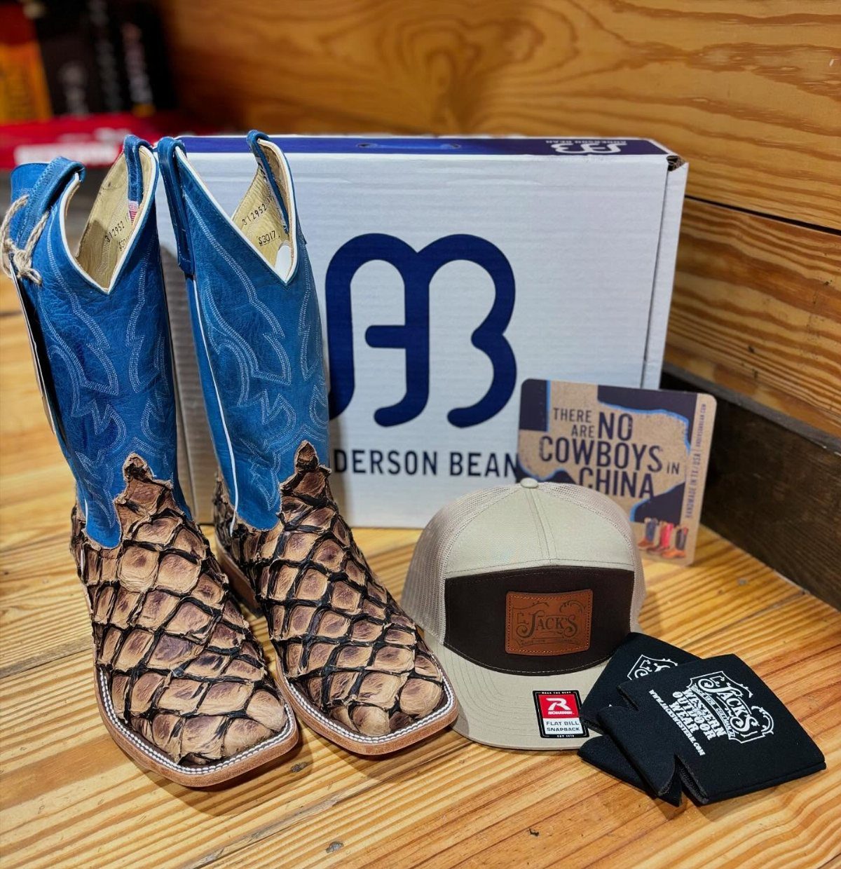 Blue and brown snakeskin cowboy boots next to an Anderson Bean branded box and a tan cap.