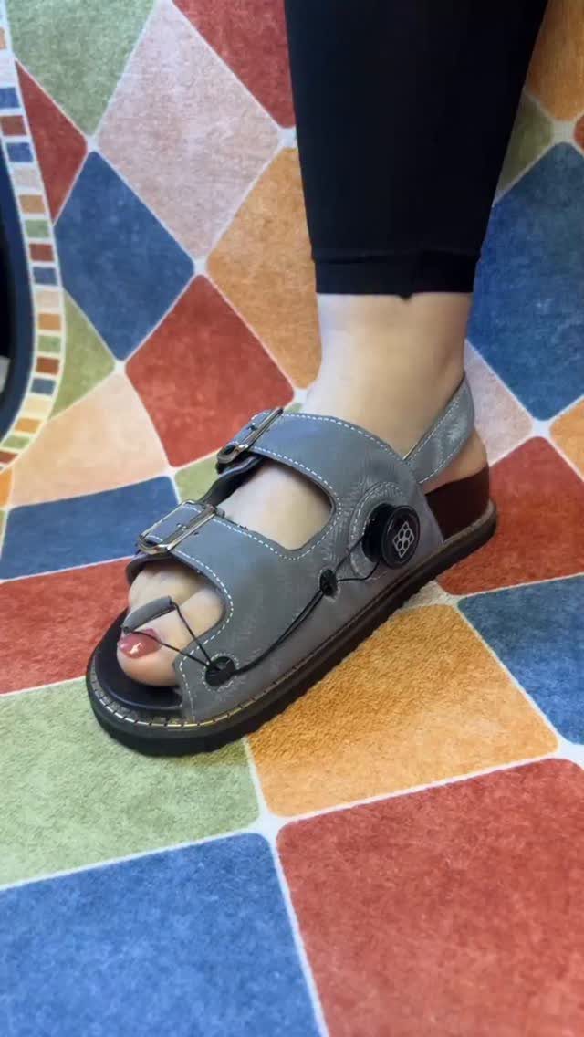 Grey leather sandals with adjustable straps and a dial closure on a person's foot.