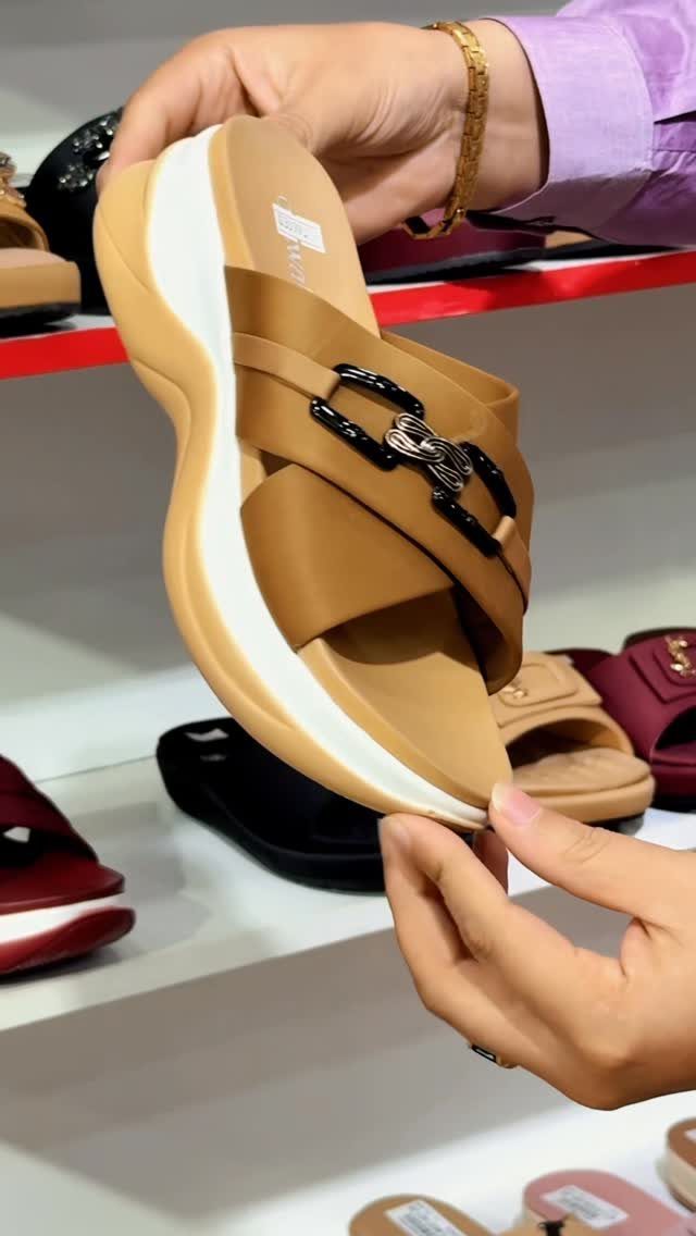 Tan slide sandals with thick white cushioned soles being held by hands in a retail store.