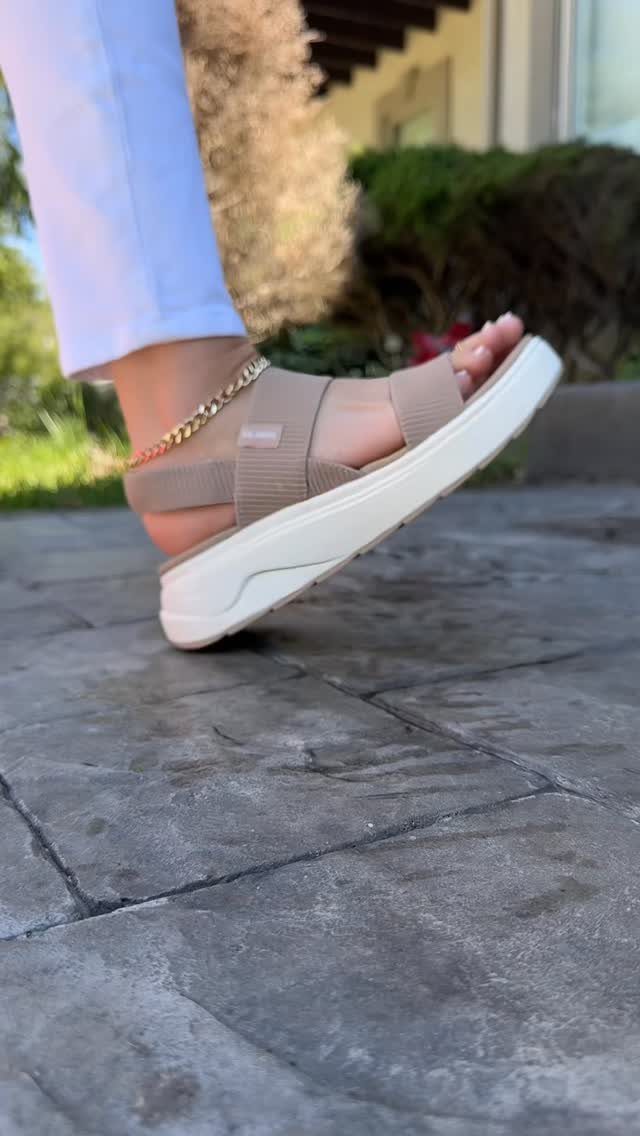 A person wearing tan platform sandals with wide straps walking on a stone patio outdoors.