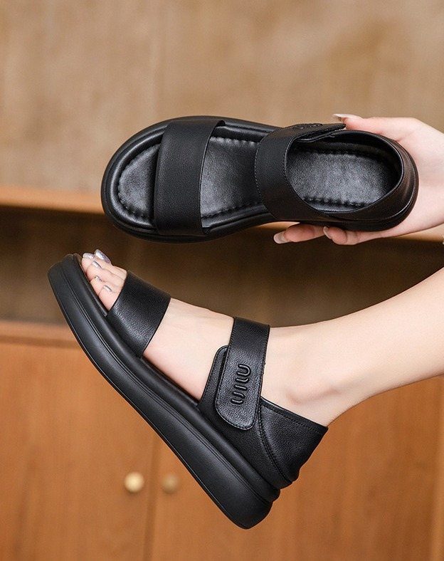 A person wearing a black leather sandal with wide straps and a thick sole.