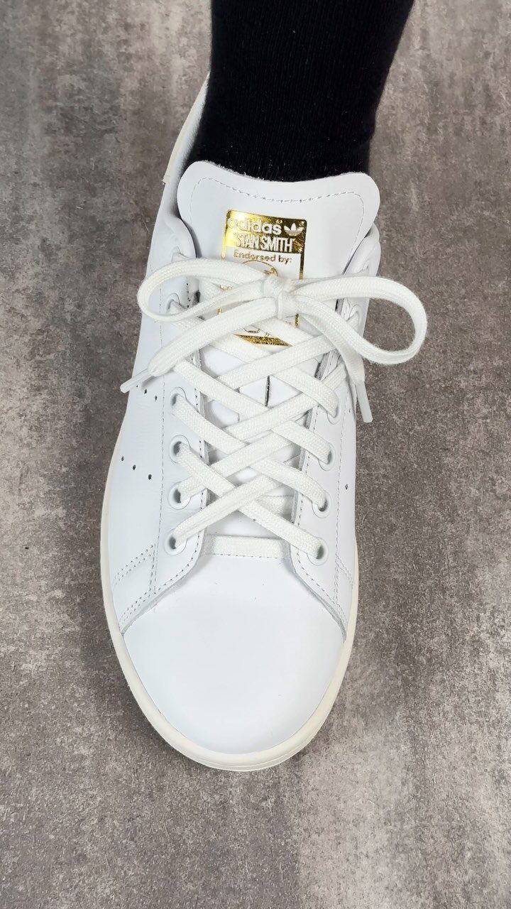 White Adidas Stan Smith sneaker with gold branding on the tongue worn with a black sock.