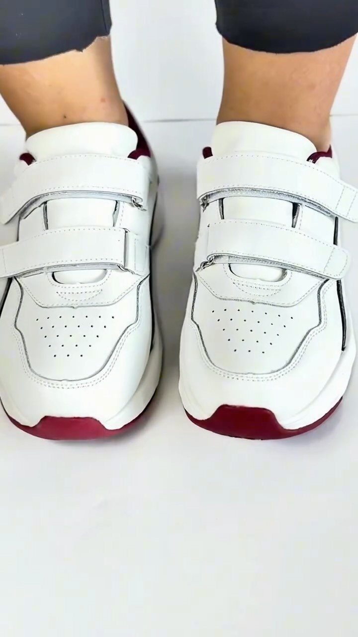 White chunky sneakers with velcro straps and red soles worn by a person.