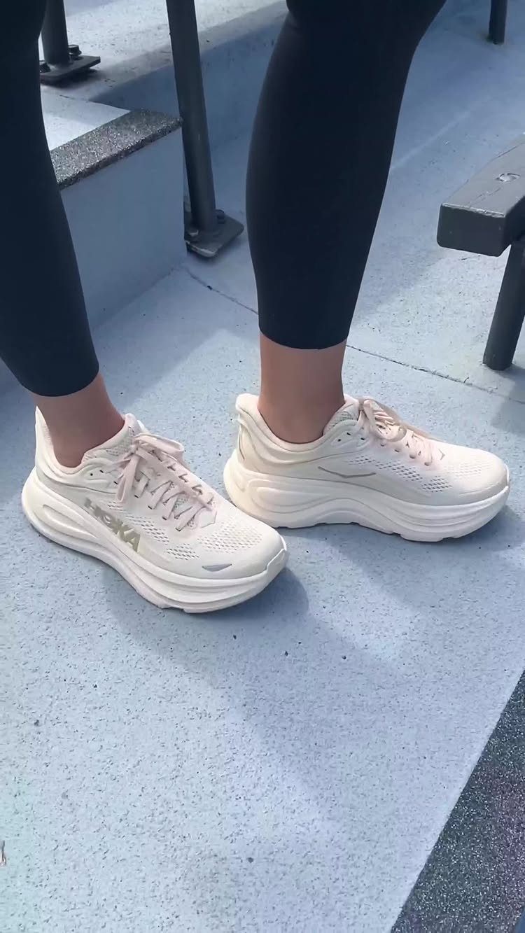 Cream Hoka Clifton sneakers worn by a person in black leggings on blue stairs.